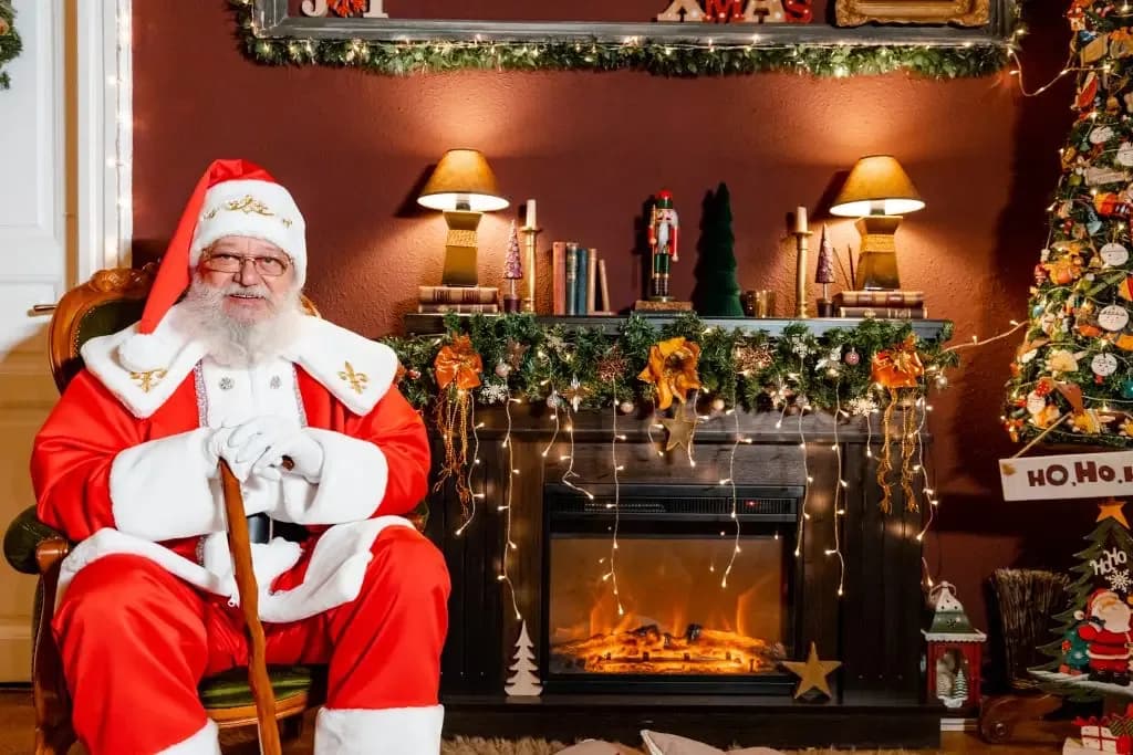Moș Crăciun într-o cameră decorată de Crăciun, lângă șemineu